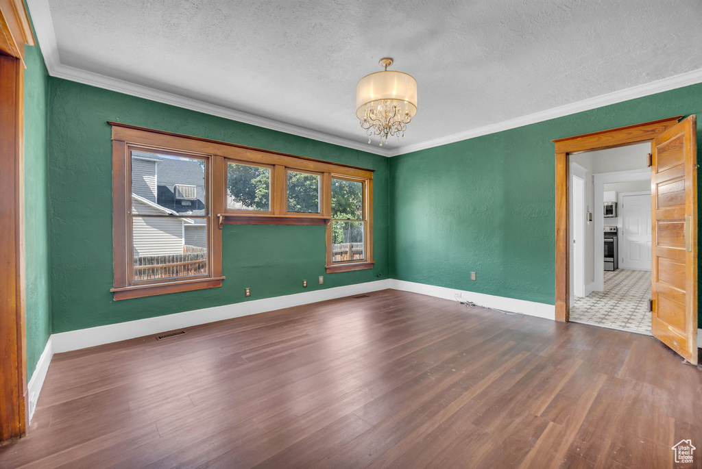 Unfurnished room featuring a textured ceiling, a chandelier, wood finished floors, ornamental molding, and a textured wall