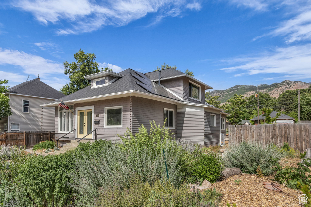 View of front of house with solar panels, a mountain view, french doors, and roof with shingles