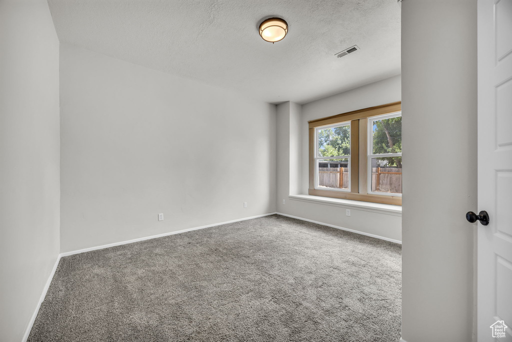 Carpeted empty room with a textured ceiling and baseboards