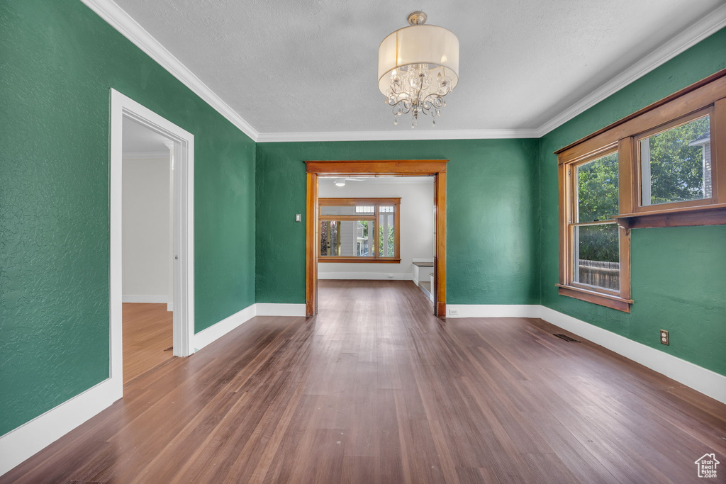 Unfurnished room with healthy amount of natural light, a chandelier, wood finished floors, ornamental molding, and a textured wall