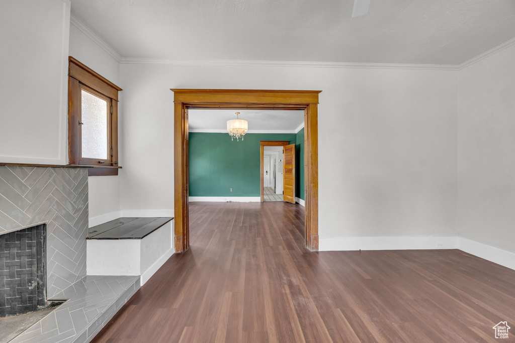 Unfurnished living room featuring wood finished floors, ornamental molding, a fireplace, and a chandelier