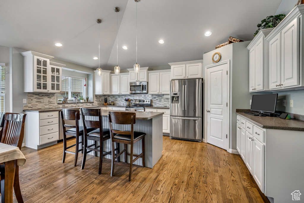 Kitchen with stainless steel appliances, dark countertops, a kitchen island, white cabinetry, and a kitchen breakfast bar