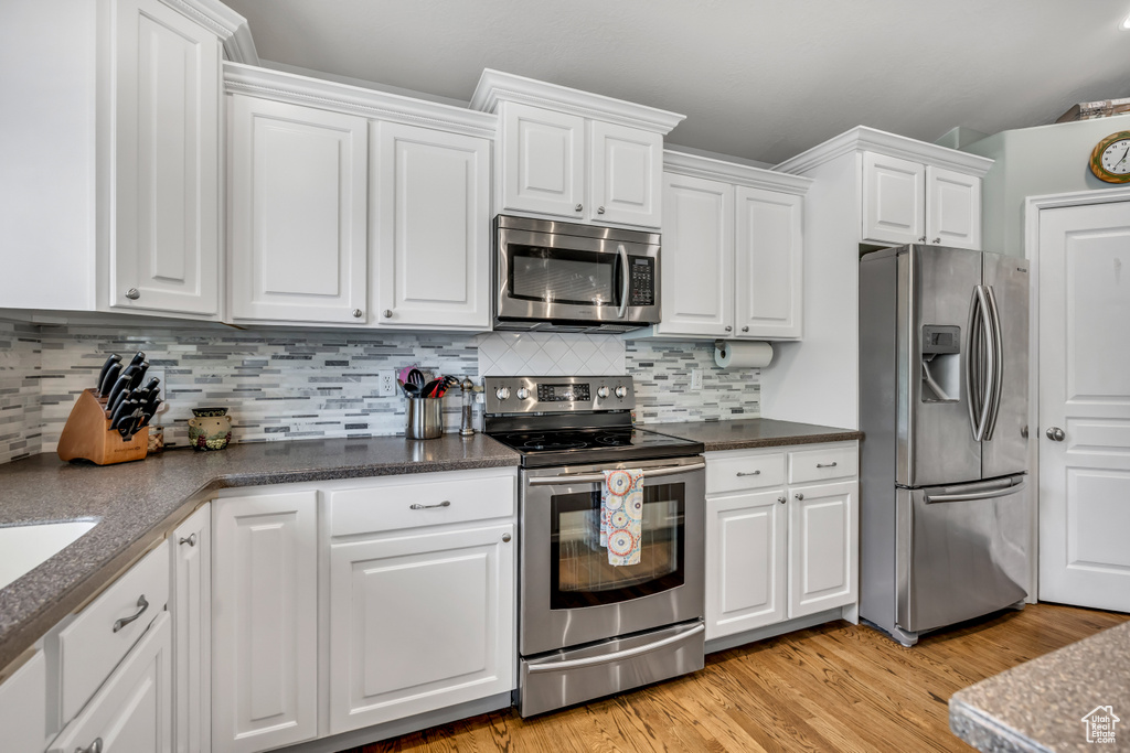 Kitchen with stainless steel appliances, white cabinetry, light wood-type flooring, and backsplash
