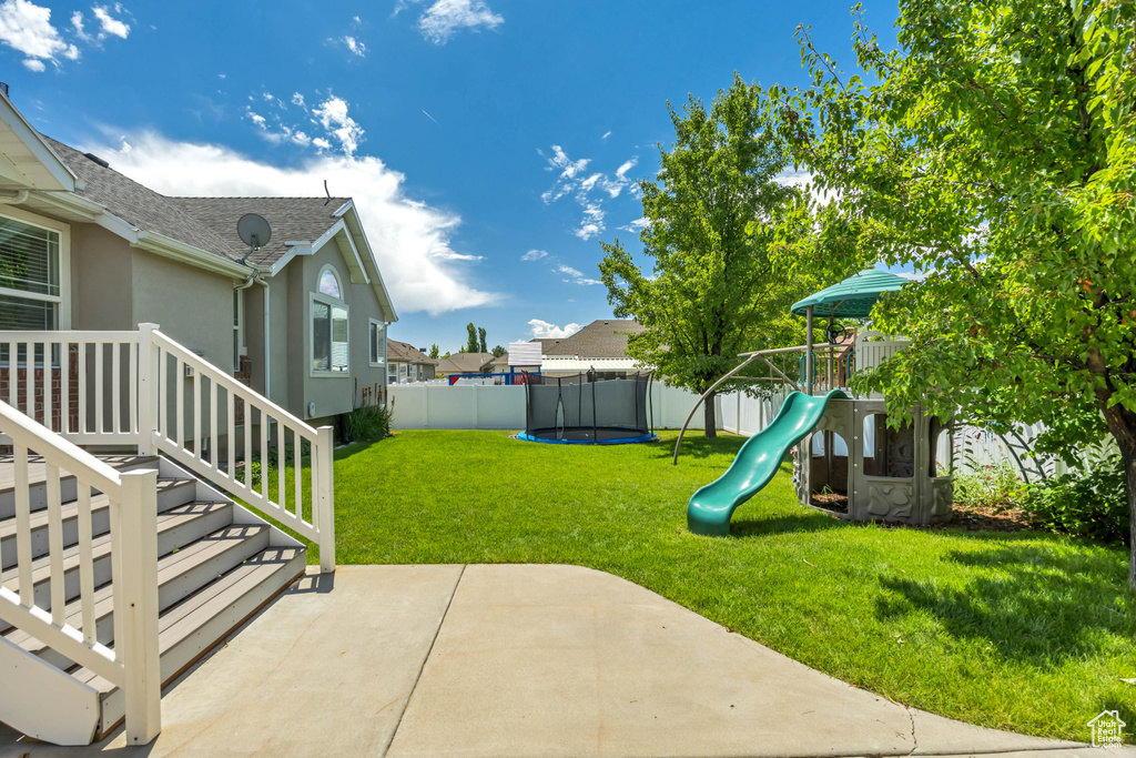 Fenced backyard with a playground, a patio area, a trampoline, and a residential view