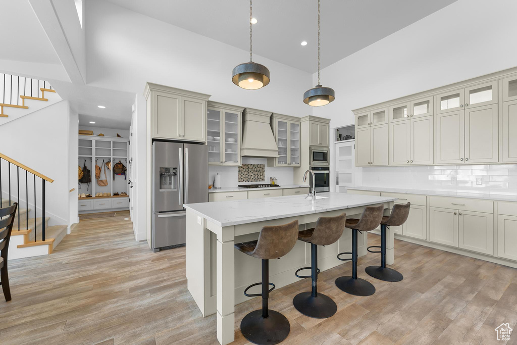 Kitchen with appliances with stainless steel finishes, high vaulted ceiling, custom exhaust hood, an island with sink, and a breakfast bar area
