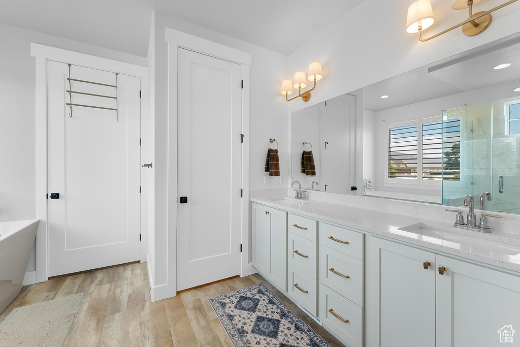 Bathroom with a shower stall, wood finished floors, double vanity, a soaking tub, and recessed lighting