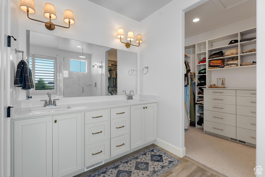 Bathroom with a shower stall, a spacious closet, double vanity, and wood finished floors