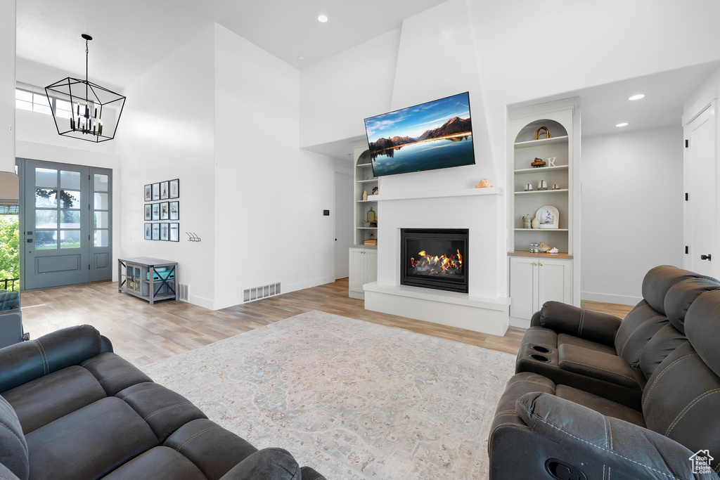 Living area featuring wood finished floors, a high ceiling, a chandelier, a glass covered fireplace, and built in features