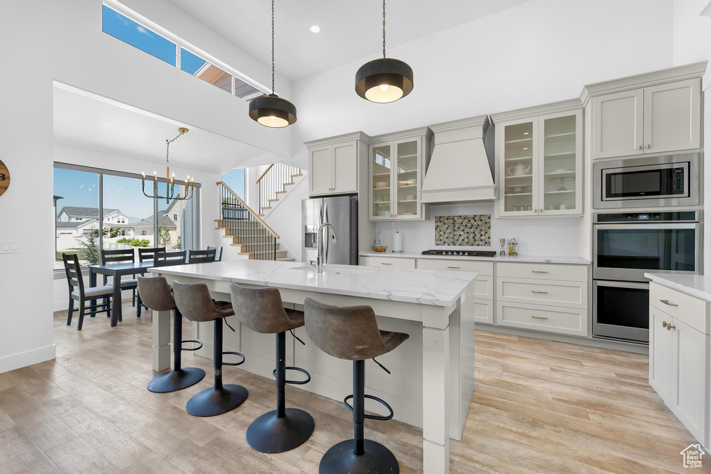 Kitchen featuring custom exhaust hood, stainless steel appliances, a kitchen breakfast bar, an island with sink, and decorative light fixtures