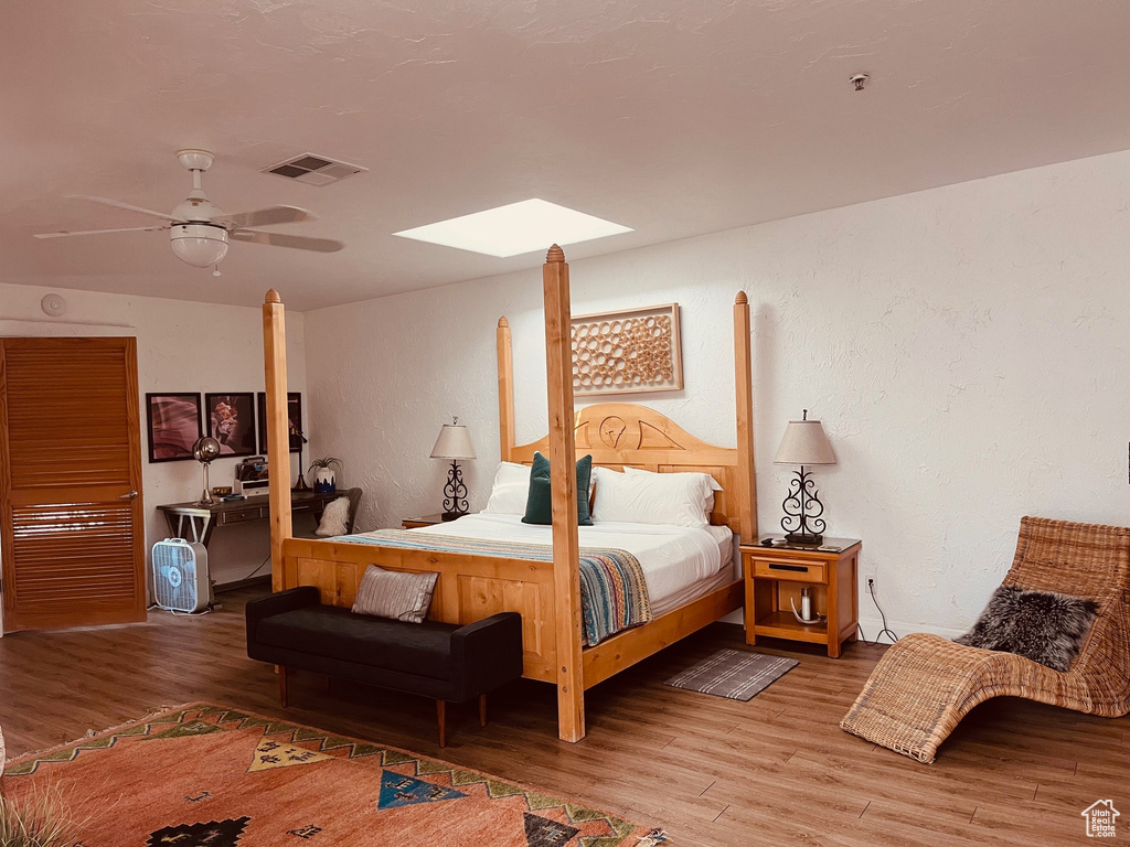 Bedroom featuring wood finished floors, a skylight, a textured wall, and a ceiling fan