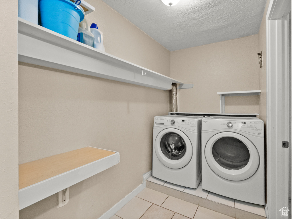 Washroom with washer and clothes dryer, light tile patterned floors, and a textured ceiling