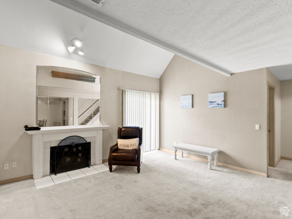 Unfurnished room featuring carpet, a textured ceiling, lofted ceiling, a tiled fireplace, and stairs