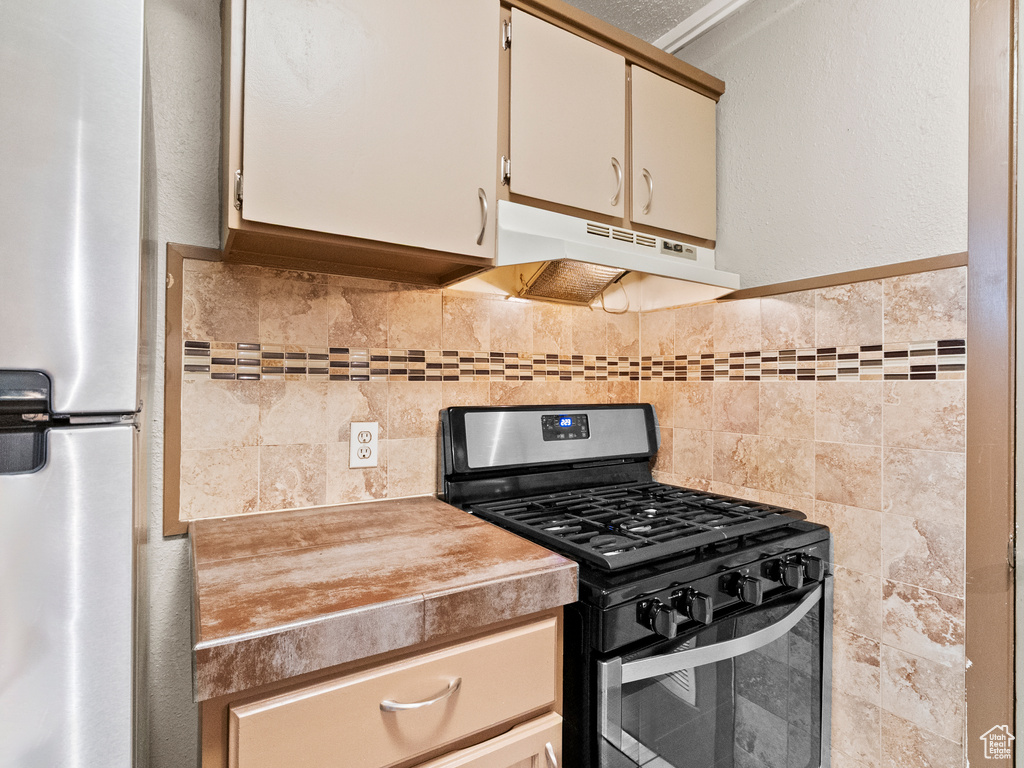Kitchen featuring gas stove, under cabinet range hood, freestanding refrigerator, and light countertops