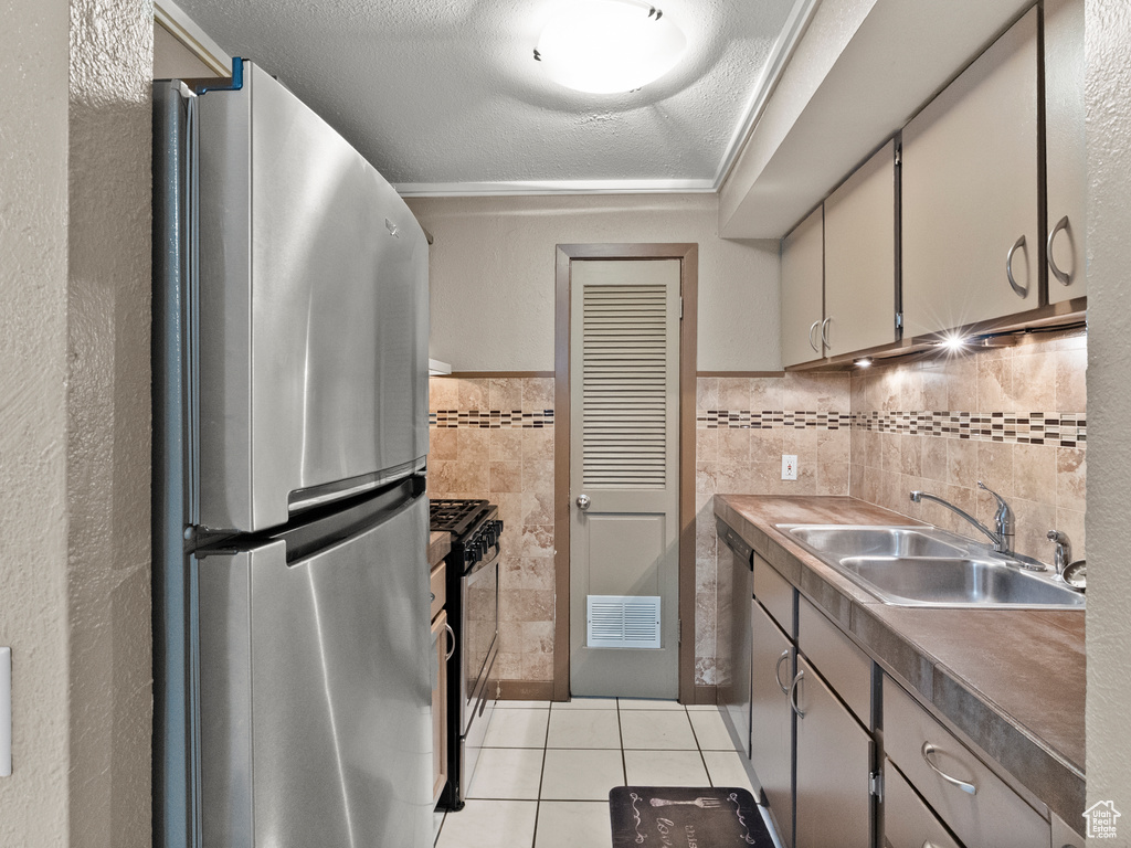 Kitchen with appliances with stainless steel finishes, light tile patterned flooring, tile walls, a textured ceiling, and a wainscoted wall