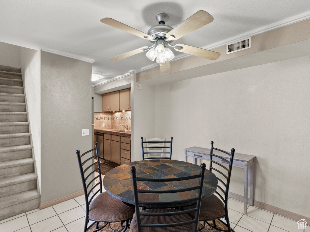 Dining room with light tile patterned floors, stairs, bar with sink, and ceiling fan