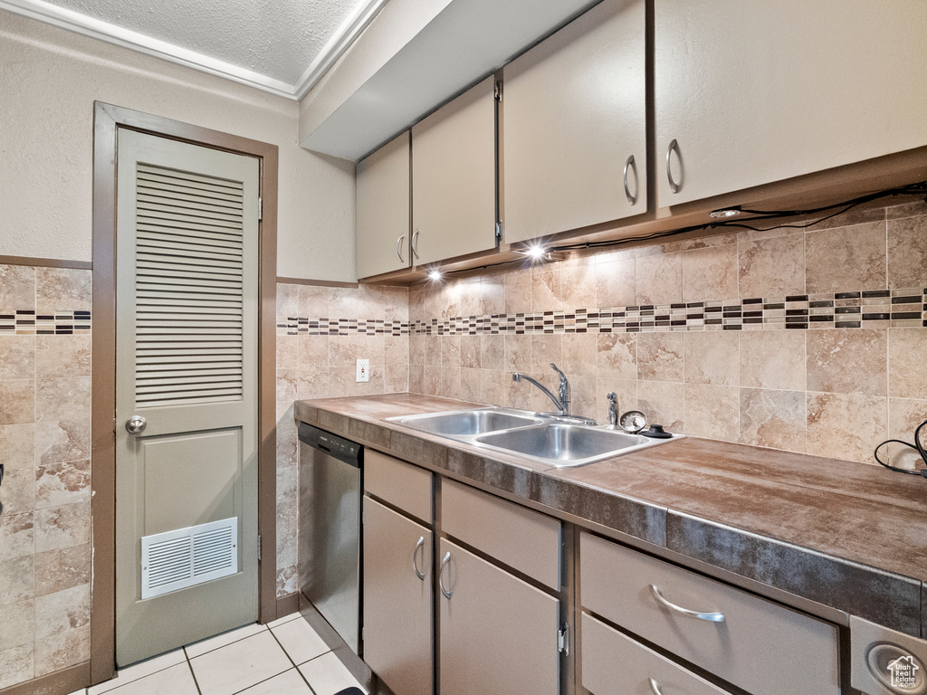 Kitchen with stainless steel dishwasher, tile walls, light tile patterned floors, and wainscoting