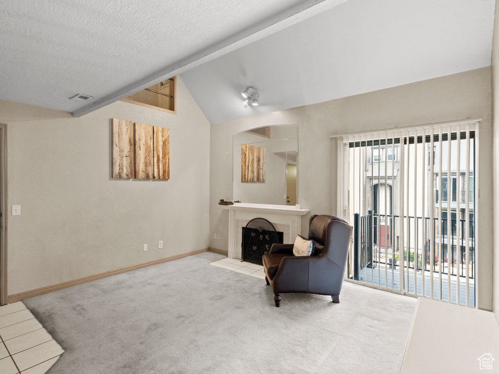 Living area with vaulted ceiling, carpet floors, a textured ceiling, and a tiled fireplace