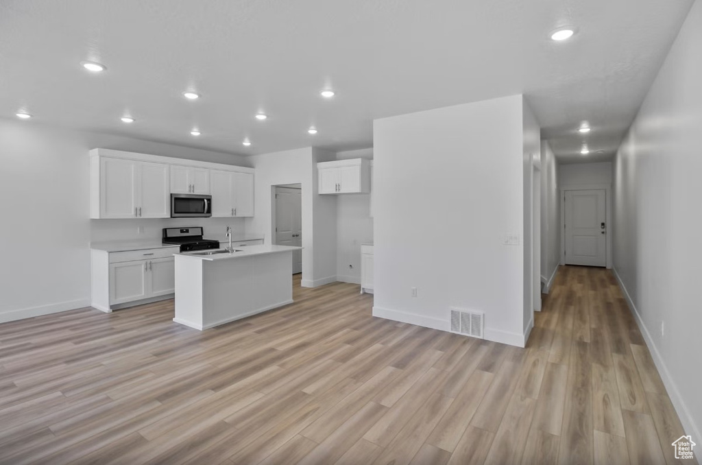 Kitchen featuring stainless steel microwave, range with gas cooktop, light wood-style floors, white cabinets, and light countertops