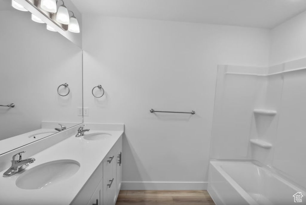 Bathroom with double vanity, wood finished floors, and washtub / shower combination