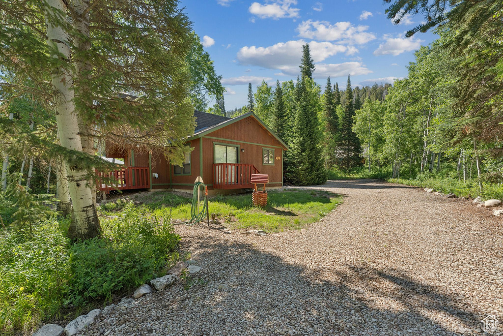 View of side of property with gravel driveway, a shingled roof, and a forest view