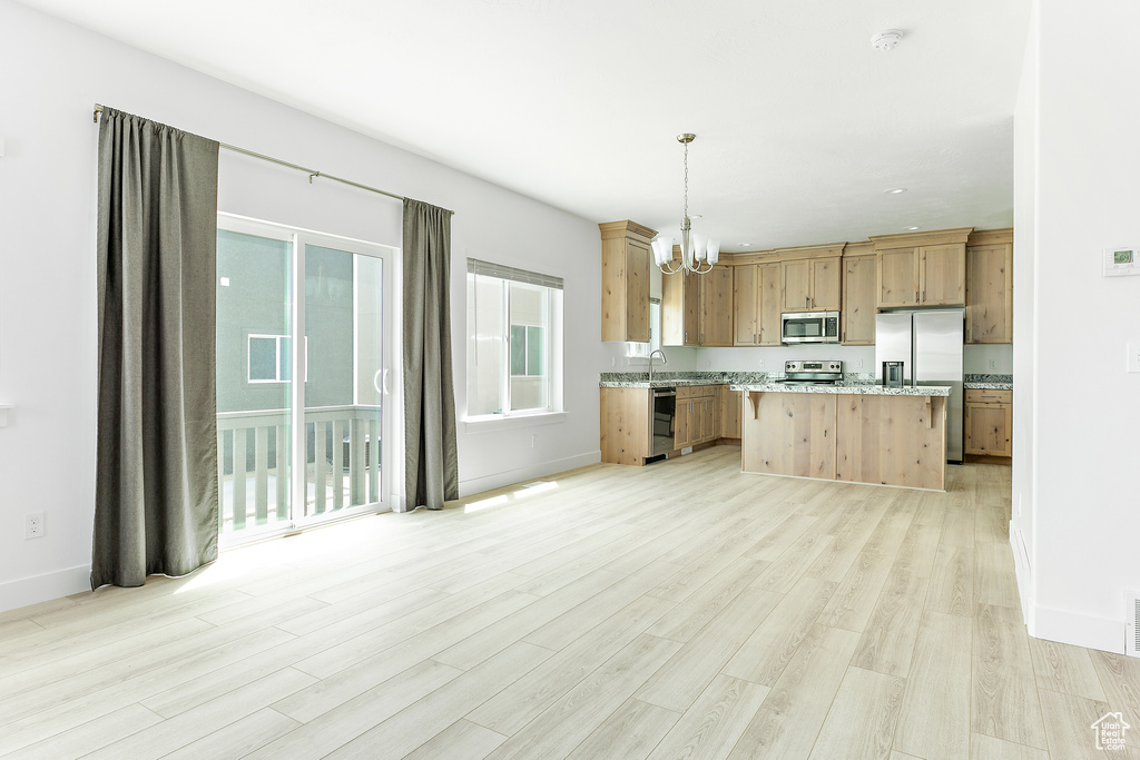Kitchen featuring stainless steel appliances, a chandelier, light wood finished floors, and decorative light fixtures