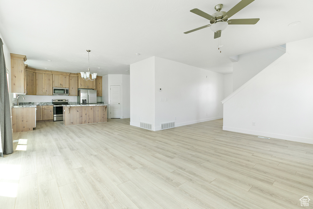 Unfurnished living room featuring a chandelier, a ceiling fan, and light wood-style floors