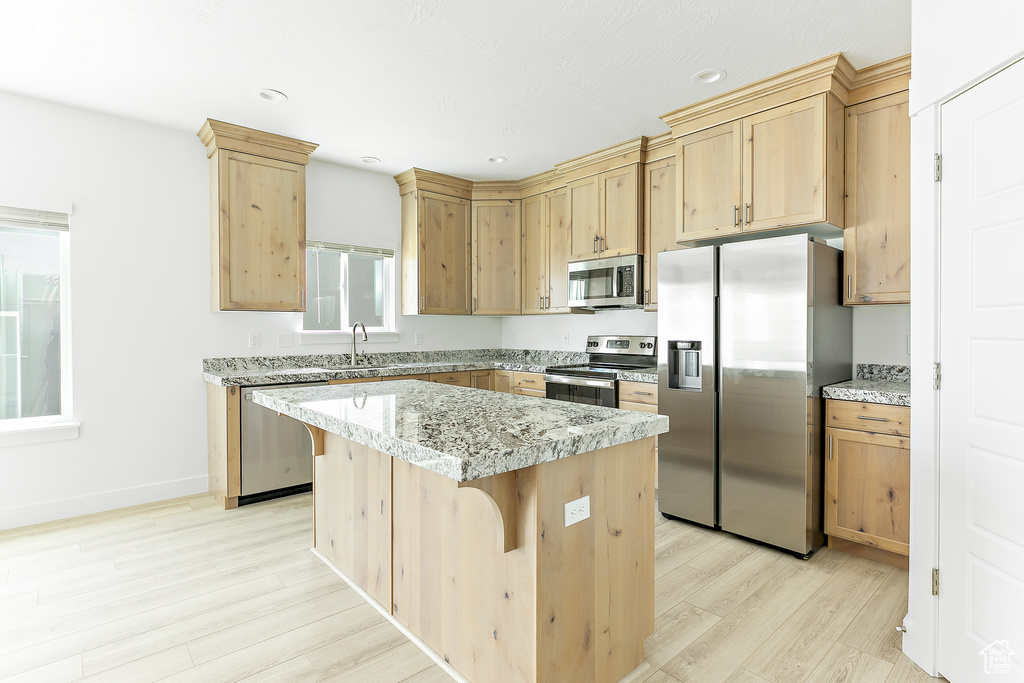 Kitchen with appliances with stainless steel finishes, light wood finished floors, light brown cabinets, a center island, and a breakfast bar