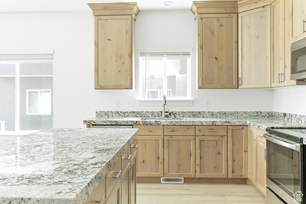 Kitchen with appliances with stainless steel finishes, light brown cabinets, light wood-style floors, and light stone countertops