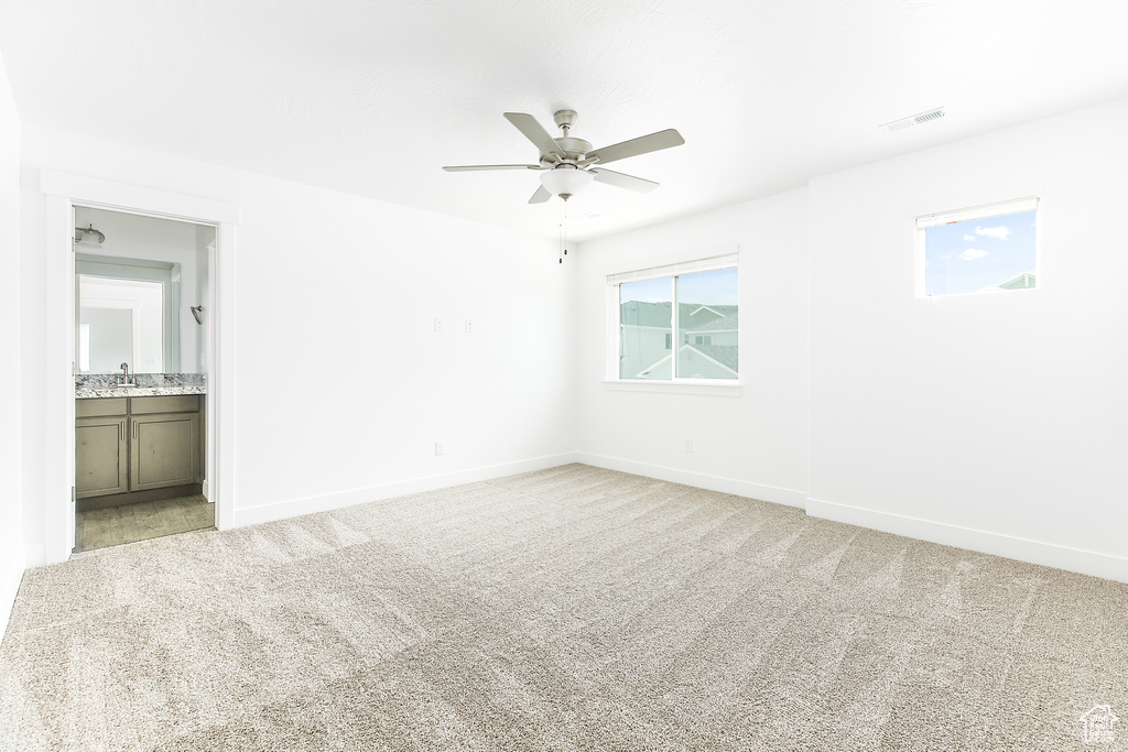 Unfurnished bedroom with light carpet, connected bathroom, and a ceiling fan