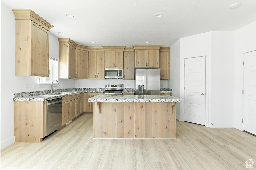 Kitchen with stainless steel appliances, light wood-style floors, a center island, light stone countertops, and recessed lighting