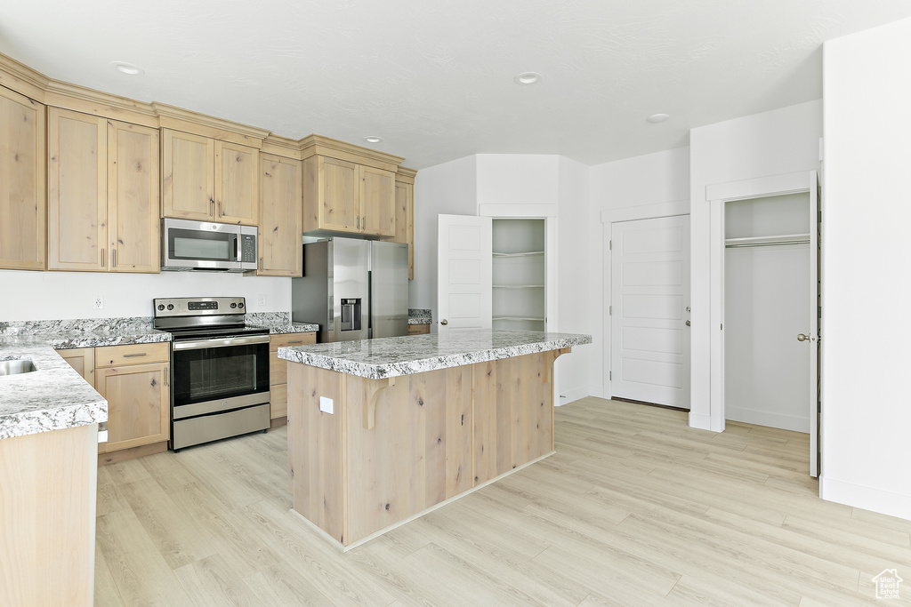 Kitchen with stainless steel appliances, light wood-style flooring, a center island, light brown cabinetry, and recessed lighting