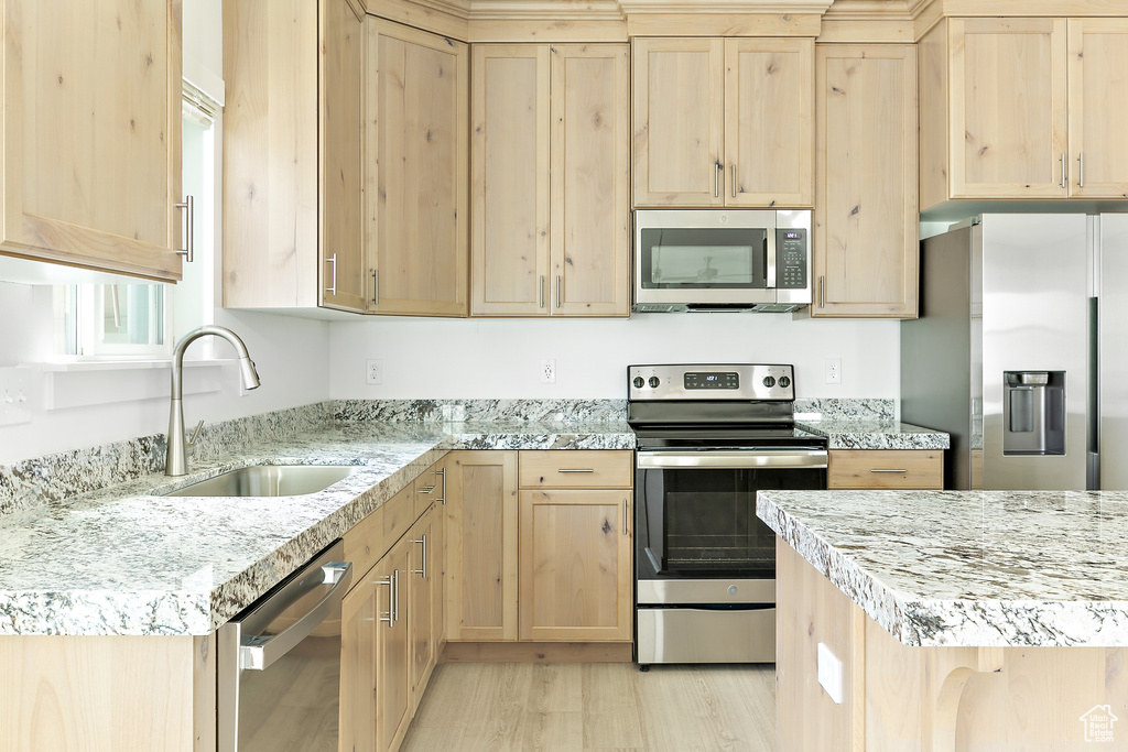 Kitchen with appliances with stainless steel finishes, light brown cabinets, light wood-style flooring, and light stone countertops