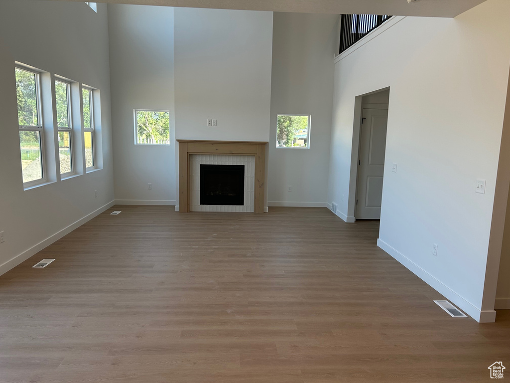 Unfurnished living room featuring a towering ceiling, a tile fireplace, and light wood-style flooring