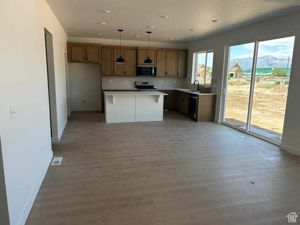 Kitchen featuring appliances with stainless steel finishes, a kitchen island, tasteful backsplash, a mountain view, and light wood-style floors
