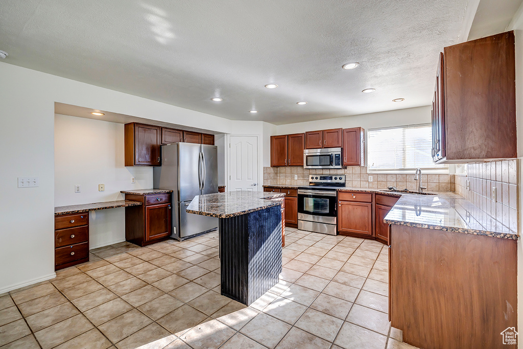 Kitchen with appliances with stainless steel finishes, tasteful backsplash, light stone countertops, light tile patterned floors, and a kitchen island