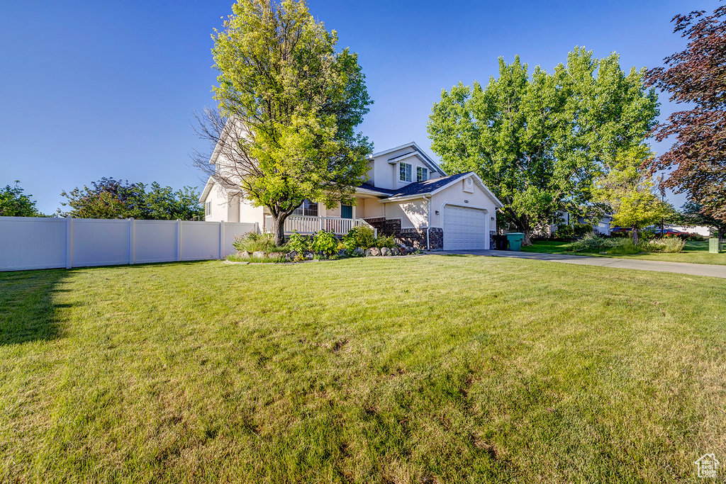 View of property hidden behind natural elements featuring driveway, an attached garage, and stucco siding