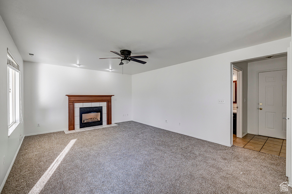 Unfurnished living room featuring light carpet, a ceiling fan, a fireplace, and light tile patterned floors