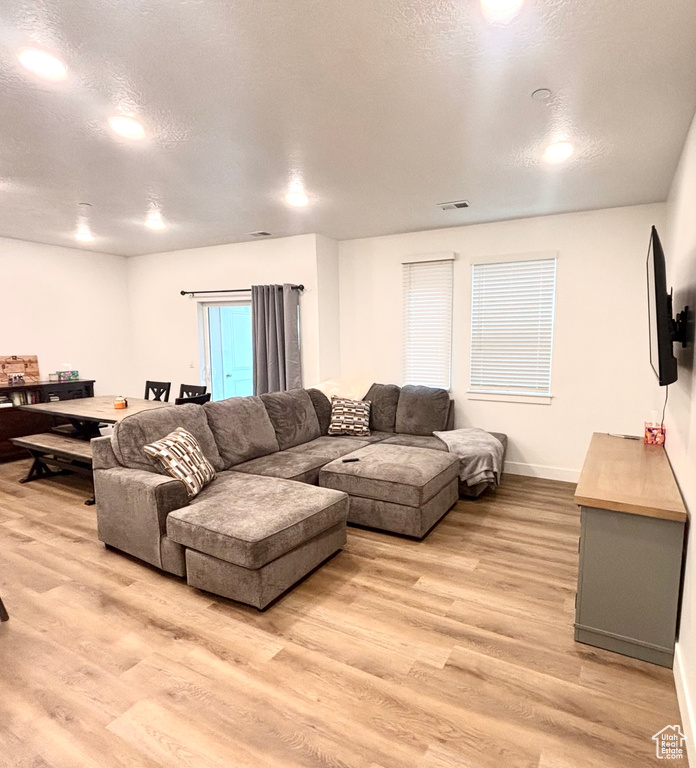 Living room with light wood-style floors, baseboards, a textured ceiling, and recessed lighting