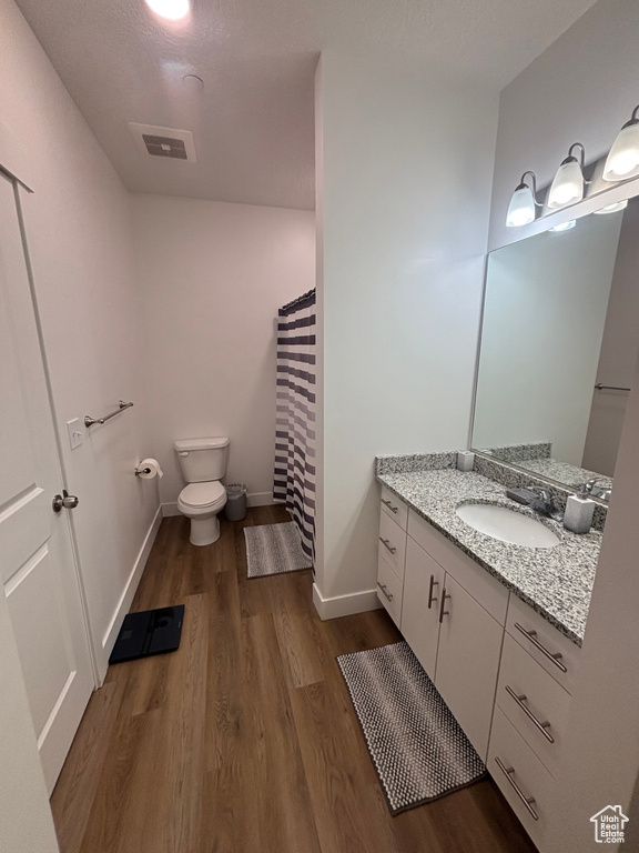 Bathroom with wood finished floors, toilet, vanity, baseboards, and a shower with shower curtain