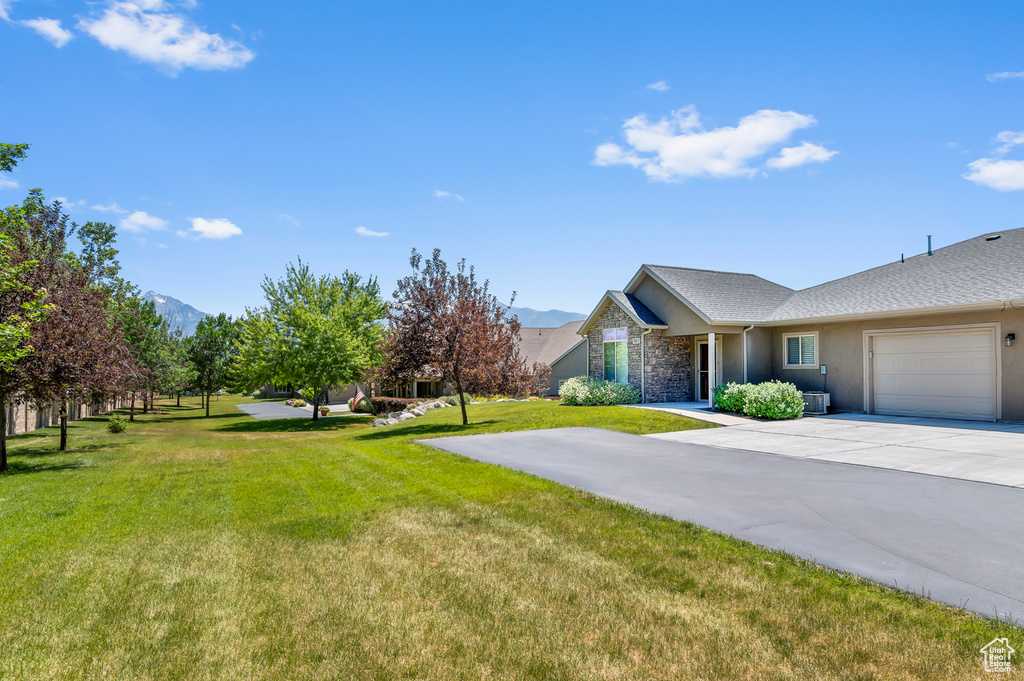 View of green lawn with an attached garage, concrete driveway, and a mountain view