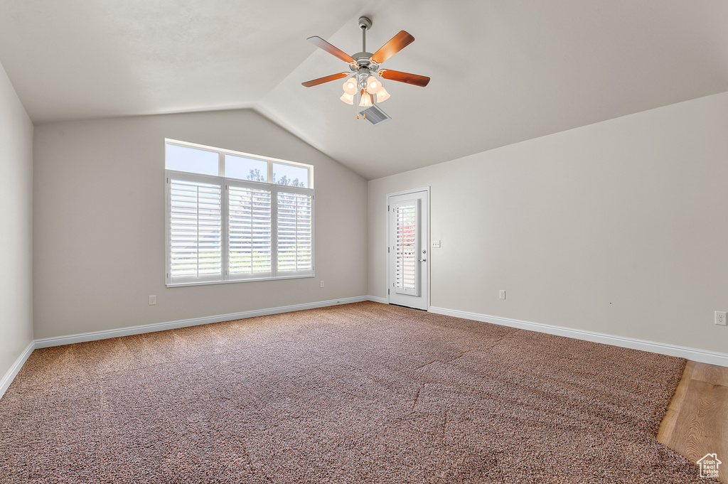 Spare room featuring a ceiling fan, plenty of natural light, lofted ceiling, and light colored carpet