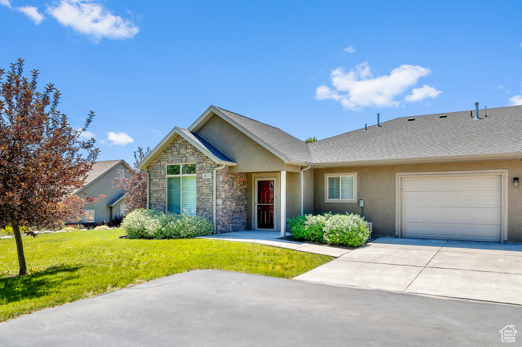 View of front of home featuring a garage, stucco siding, a front yard, concrete driveway, and stone siding