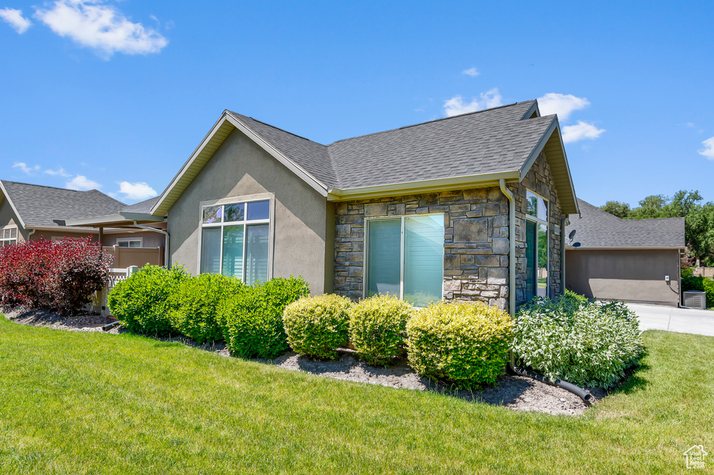 View of side of home featuring stone siding, a lawn, a shingled roof, stucco siding, and driveway