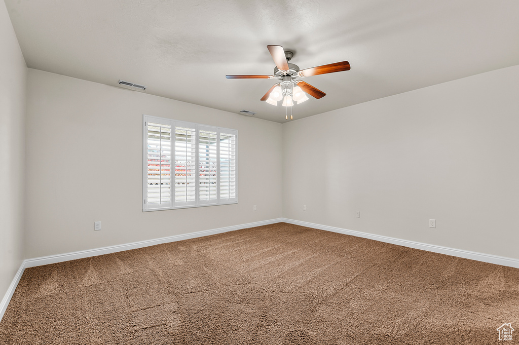 Carpeted empty room featuring a ceiling fan and baseboards