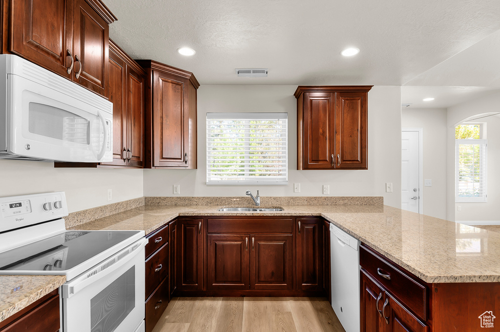 Kitchen with white appliances, a peninsula, light wood-style floors, light stone countertops, and recessed lighting