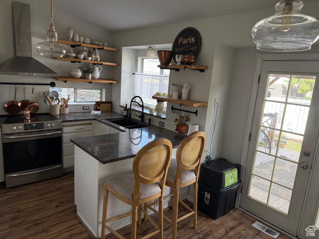 Kitchen featuring wall chimney range hood, stainless steel range with electric stovetop, open shelves, white cabinets, and a peninsula