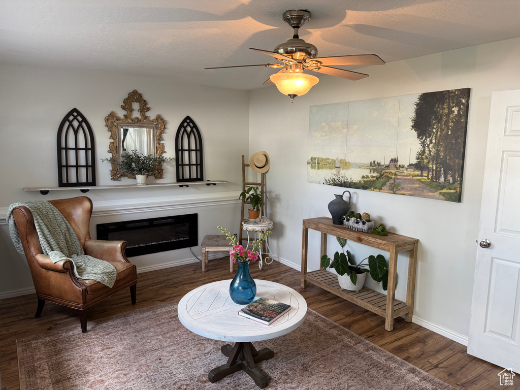 Living area featuring wood finished floors, a glass covered fireplace, and ceiling fan