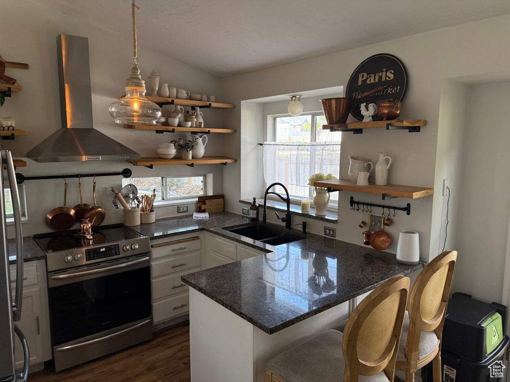 Kitchen with stainless steel electric range, open shelves, wall chimney range hood, white cabinetry, and a peninsula