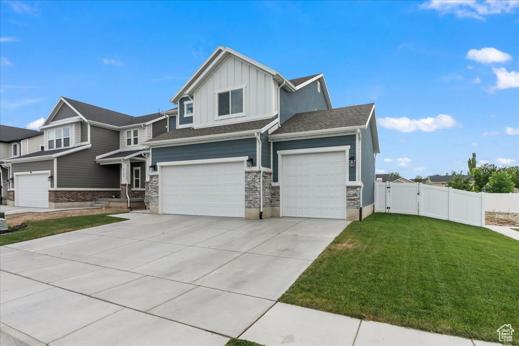 View of front facade with board and batten siding, a gate, an attached garage, driveway, and stone siding