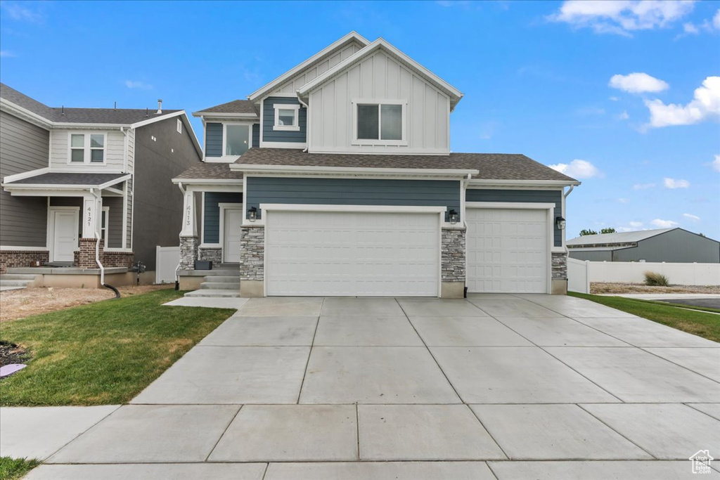 View of front of home with board and batten siding, concrete driveway, an attached garage, stone siding, and a front yard